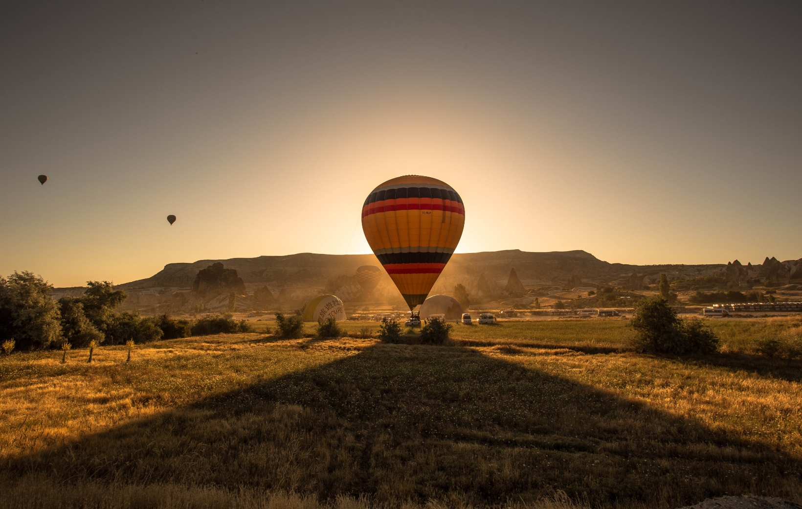 picture-colorful-hot-air-balloon-field-surrounded-by-greenery-mountains-during-sunset